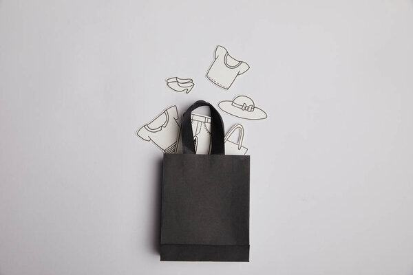 top view of black shopping bag and paper clothes on grey background, shopping concept