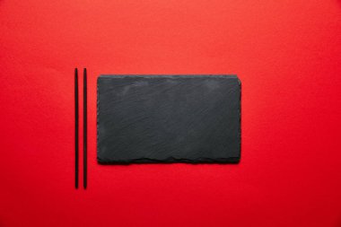 top view of empty black slate plate for sushi and chopsticks isolated on red clipart