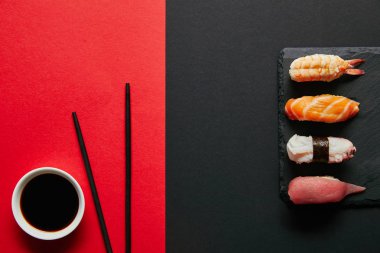 düz lay kırmızı ve siyah arka plan üzerinde siyah arduvaz plaka üzerinde kase, yemek çubukları ve nigiri suşi kümesindeki soya sosu ile