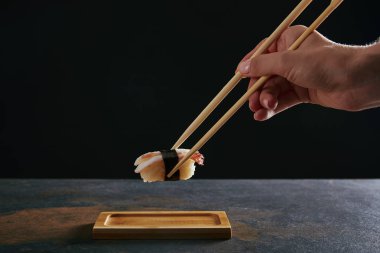 partial view of woman holding nigiri sushi with shrimp on black background clipart