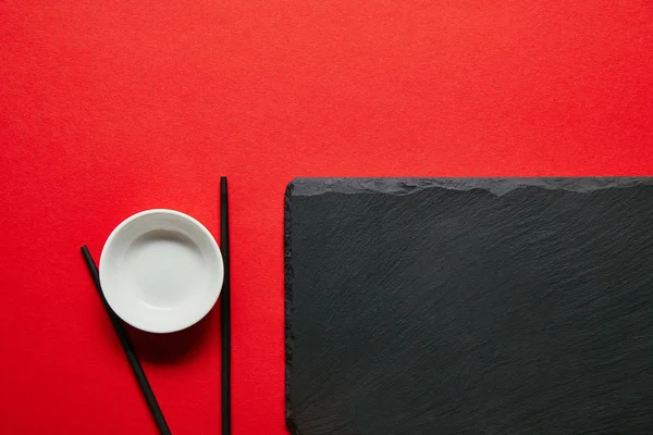 红色背景上排列的空碗 筷子和石板板的顶部视图 — 图库照片