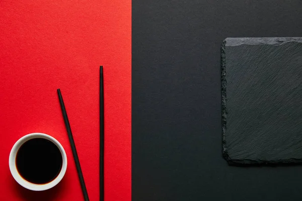 红色和黑色背景的碗 筷子和石板板上的酱油的顶部视图 — 图库照片