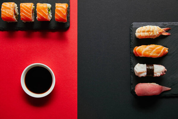 flat lay with soya sauce in bowl, sushi sets on black slate plates on red and black background