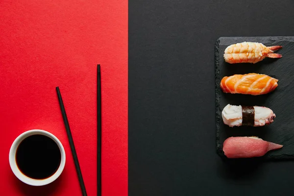 Flat lay with soya sauce in bowl, chopsticks and nigiri sushi set on black slate plate on red and black background — Stock Image Flat Lay Soya Sauce Bowl Chopsticks Nigiri Sushi Set Black Royalty Free Stock Images