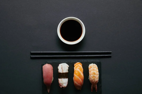 Top view of assorted nigiri sushi set, chopsticks and soya sauce on black slate plate on dark tabletop — Stock Image Top View Assorted Nigiri Sushi Set Chopsticks Soya Sauce Black Royalty Free Stock Photos