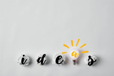 row of light bulb with crumpled papers and ideas word on white surface clipart