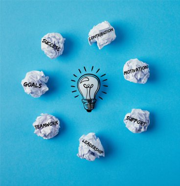 top view of light bulb surrounded with crumpled papers with business ideas on blue surface clipart