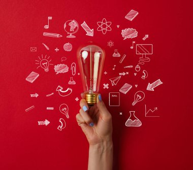 cropped shot of woman holding vintage incandescent lamp with business icons on red surface clipart