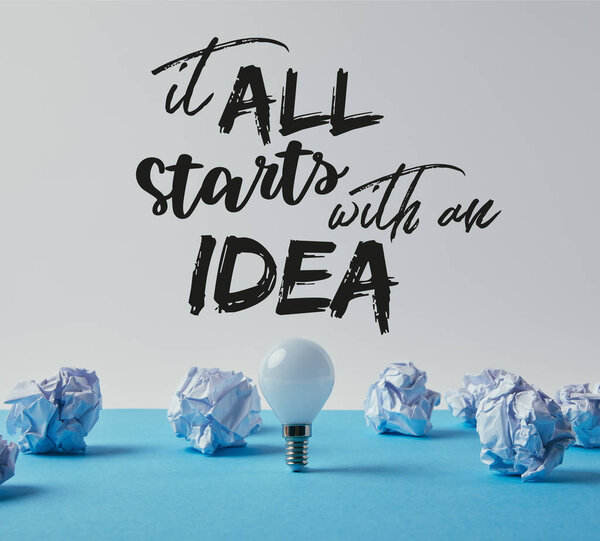 light bulb with crumpled papers on blue surface with "it all starts with an idea" inspiration 