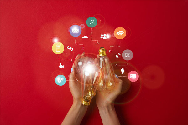 woman holding vintage incandescent lamps with business icons on red tabletop