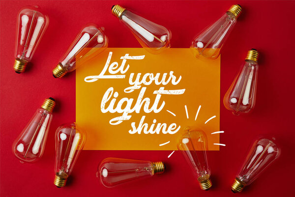 top view of vintage incandescent lamps on red surface with yellow paper and "let your light shine" inspiration