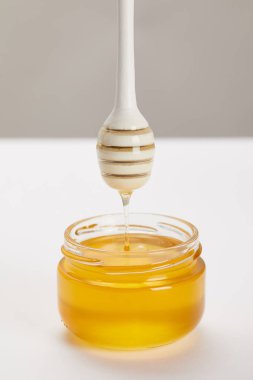 close up view of wooden honey deeper with organic honey and glass jar on grey background clipart