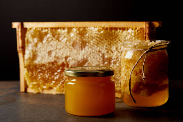 закрытый вид стеклянных банок с медом и пчелиным воском на черном фоне

