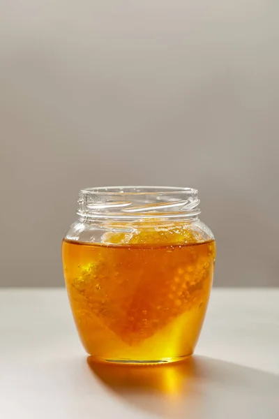 灰色の背景に蜂蜜と蜜蝋で開かれたガラス瓶のビューをクローズ アップ  — 無料ストックフォト
