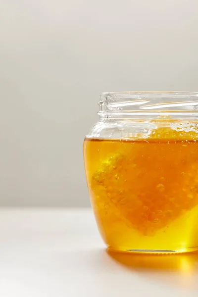 灰色の背景に蜂蜜と蜜蝋で開かれたガラス瓶のビューをクローズ アップ  — 無料ストックフォト