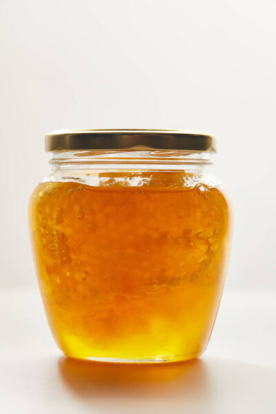 close up view of honey and beeswax in glass jar on white background