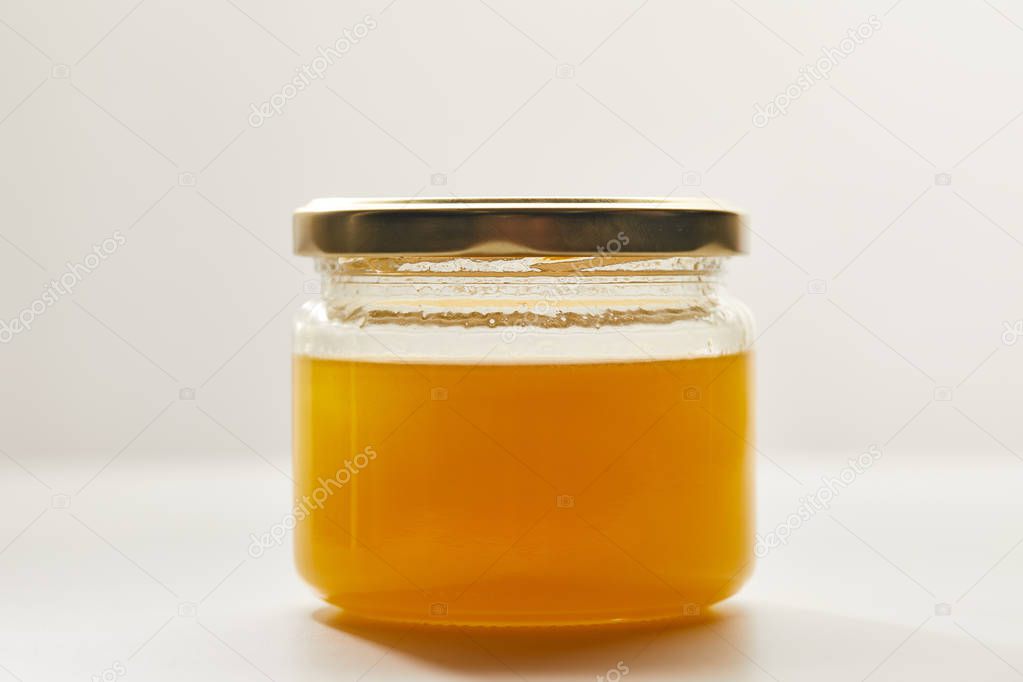 close up view of sweet organic honey in glass jar on white surface