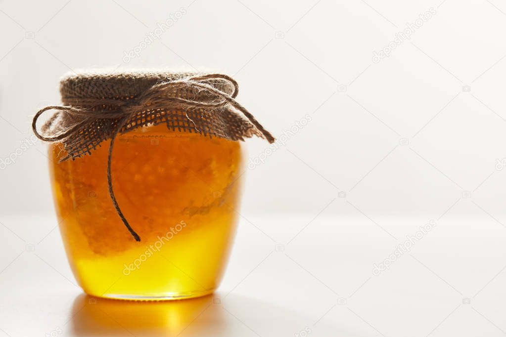 close up view of honey and beeswax in glass jar on white background