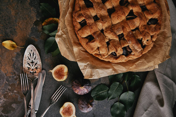 flat lay with homemade pie on baking paper, antique cutlery and fresh figs on dark tabletop