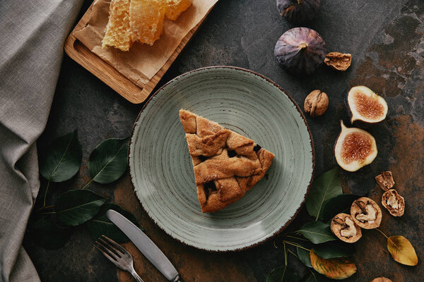 flat lay with piece of pie on plate, beeswax, figs and cutlery on grungy tabletop