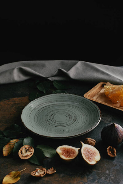close up view of empty plate, hazelnuts, honey and figs arranged on grungy tabletop with black background