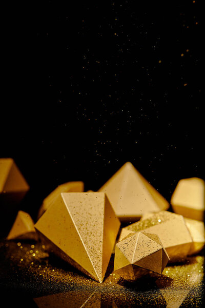 close-up view of shiny faceted golden pieces and dust on black  