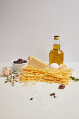 Zeytinyağı, pişmemiş makarna, biberiye ve makarna üzerine beyaz masa üstü yemek pişirmek için peynir görünümünü kapat