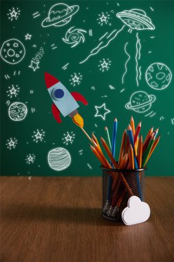 renkli kalemler, roket, bulut ahşap masa üzerinde işaretiyle kara tahta arka plan ile evren kutsal kişilerin resmi