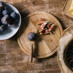 Pile of figs in bowl and on cutting board on rustic wooden table during pie preparation