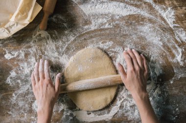cropped shot of woman preparing dough with rolling pin on rustic wooden table clipart