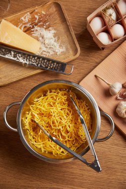 spagetti makarna üzerine ahşap masa için malzemeler ile çevrili metal kevgir içinde üstten görünüm