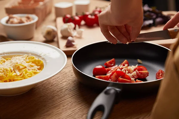 パスタを調理中のフライパンにトマトとニンニクを入れて女性のクロップ撮影 — ストック写真