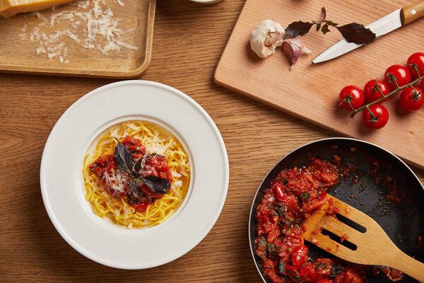 top view of plate of pasta and frying pan of tomato sauce on wooden table