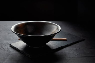 close-up view of empty bowl and chopsticks on black slate board clipart