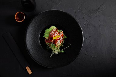 top view of delicious traditional japanese dish with seafood, avocado and herbs on black plate clipart