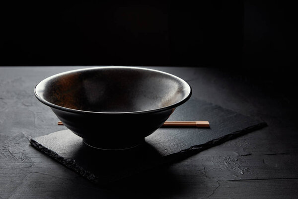 close-up view of empty bowl and chopsticks on black slate board