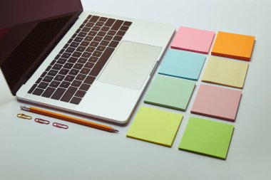 laptop, set of colored paper stickers, pencil and paper clips on white tabletop 