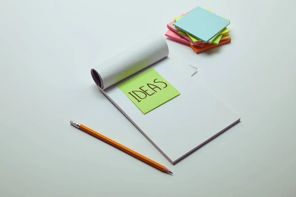 Papieraufkleber Mit Wortideen Notizbuch Bleistift Und Papierstapel Auf Weißer Tischplatte — Stockfoto