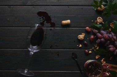 top view of glass with red wine, cork and grapes with nuts on wooden surface  clipart