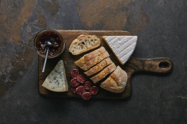 Ahşap kesme tahtası üzerinde dilimlenmiş ekmek, lezzetli peynir, salam ve reçel üstten görünüm