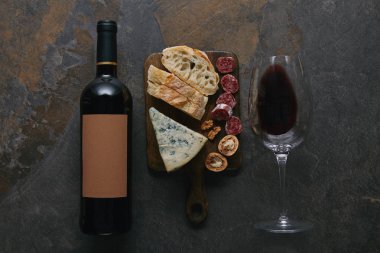 kesme tahtası üzerinde şişe ve kadeh kırmızı şarap ve lezzetli aperatifler üstten görünüm