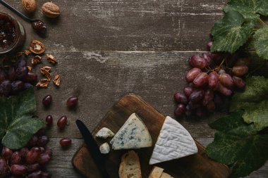 top view of fresh ripe grapes with green leaves, walnuts, delicious  cheese and jam on wooden table   clipart