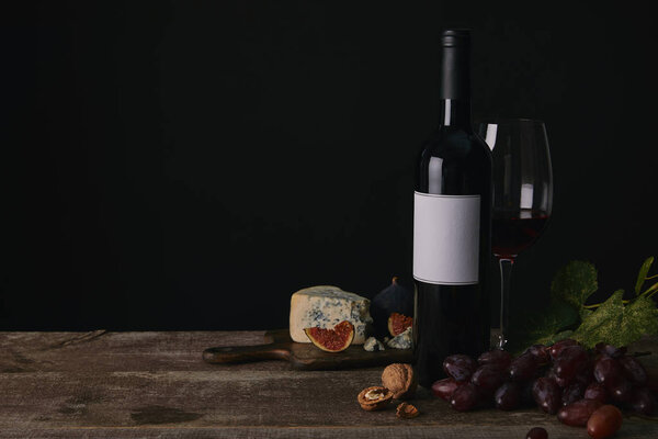 bottle and glass of red wine, grapes and cheese on wooden table