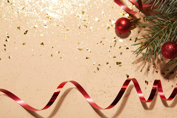 красные блестящие рождественские шары, красная волнистая лента и сосновая ветвь на блестящей поверхности
