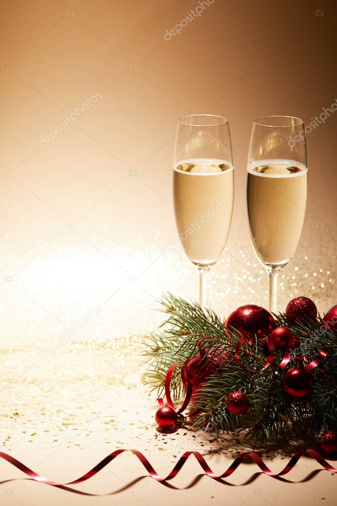 two glasses of champagne, red shiny christmas balls and pine branch on glittering tabletop