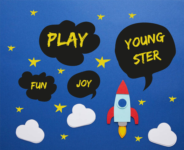 clouds and rocket on blue paper background with play, joy, fun and youngster words