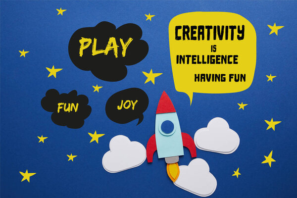 clouds and rocket on blue background with "creativity is intelligence, having fun" lettering