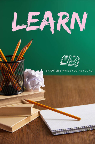 книги, тетрадь, скомканная бумага и карандаши на деревянном столе с надписью "Учитесь - наслаждайтесь жизнью, пока молоды"
