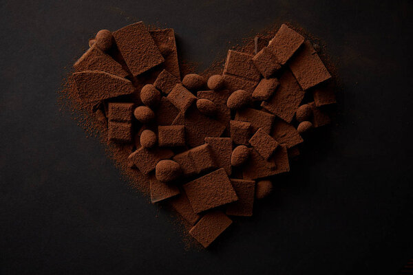 top view of tasty chocolate with nuts and cocoa powder arranged in shape of heart on black