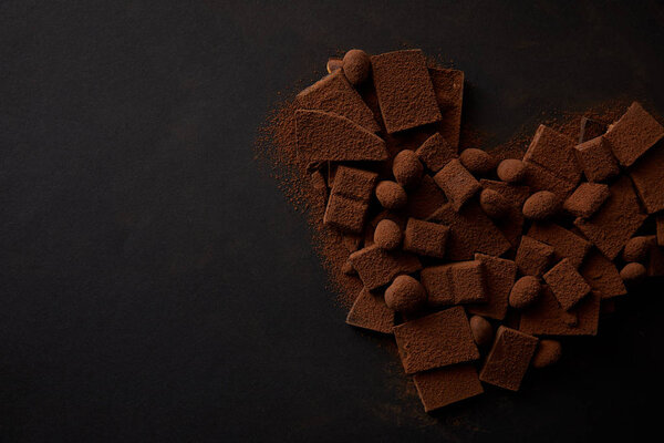 top view of delicious chocolate pieces with nuts and cocoa powder arranged in shape of heart on black background